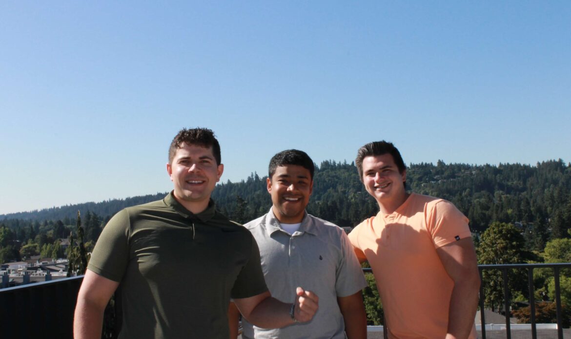 An image of three people smiling with a mountain view behind them