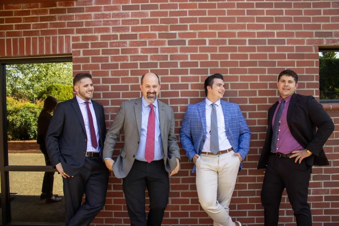 Image of four smiling men standing in front of a brick building